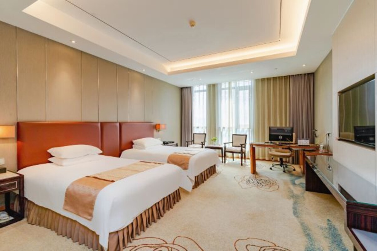 Een hotelkamer met twee bedden, een bureau, een televisie en een groot raam.