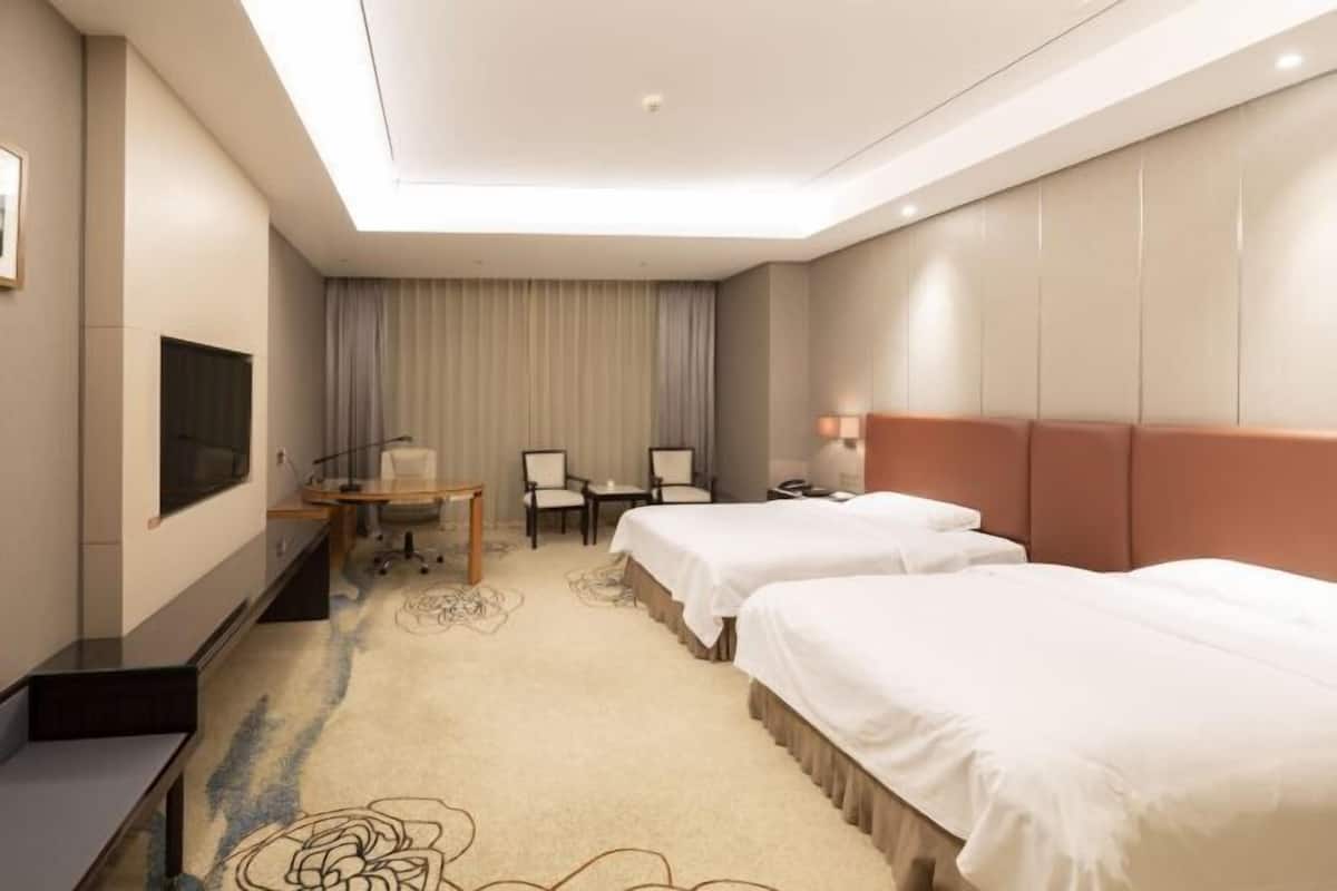 A hotel room with two beds, a desk, a chair, a TV, and a large window with curtains.