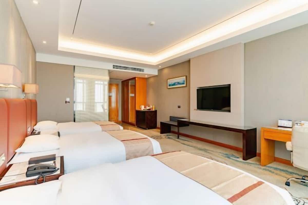 A hotel room with three beds, a TV, a desk, and a chair.