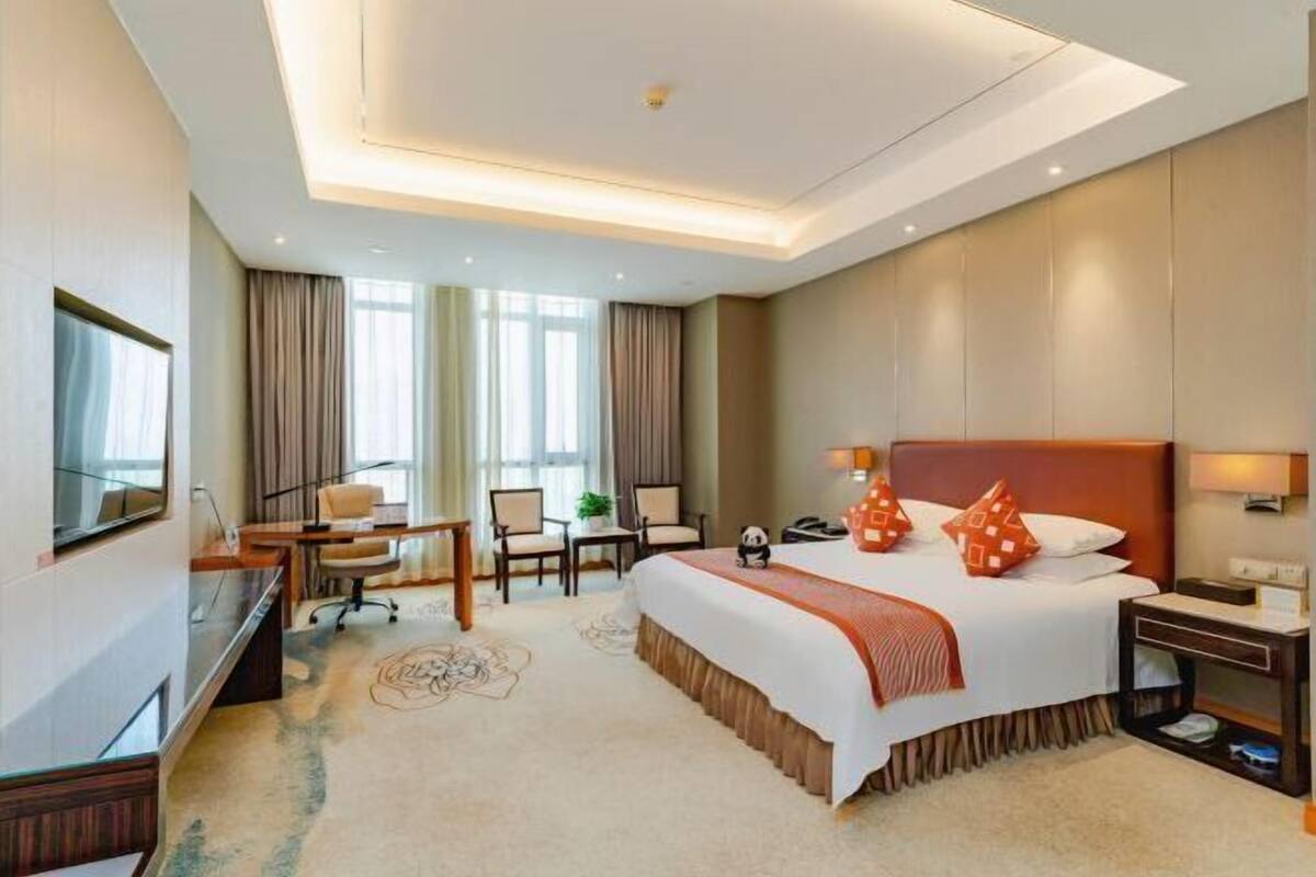 A hotel room with a large bed, a desk with a chair, a TV, and a window with curtains.