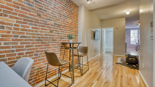 A modern living space with a brick wall, wooden flooring, and a small table with two chairs. - Charming Federal Hill! One Bedroom With Vibes (Baltimore)