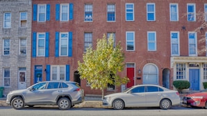 A row of townhouses with a tree in the middle, parked cars on the street, and a clear blue sky. - Charming Federal Hill! One Bedroom With Vibes (Baltimore)