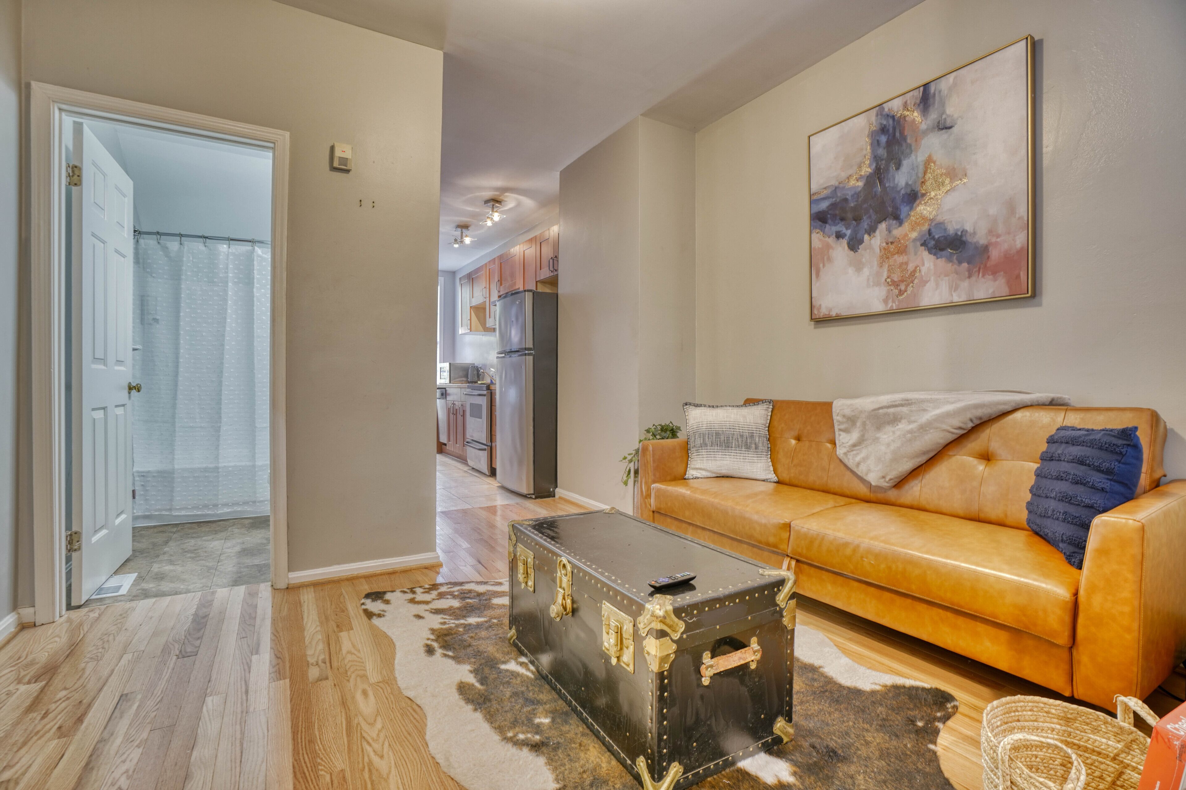A living room with a leather sofa, a vintage trunk, and a modern abstract painting.