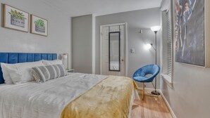 A bedroom with a bed, a chair, a painting, and a door. - Charming Federal Hill! One Bedroom With Vibes (Baltimore)