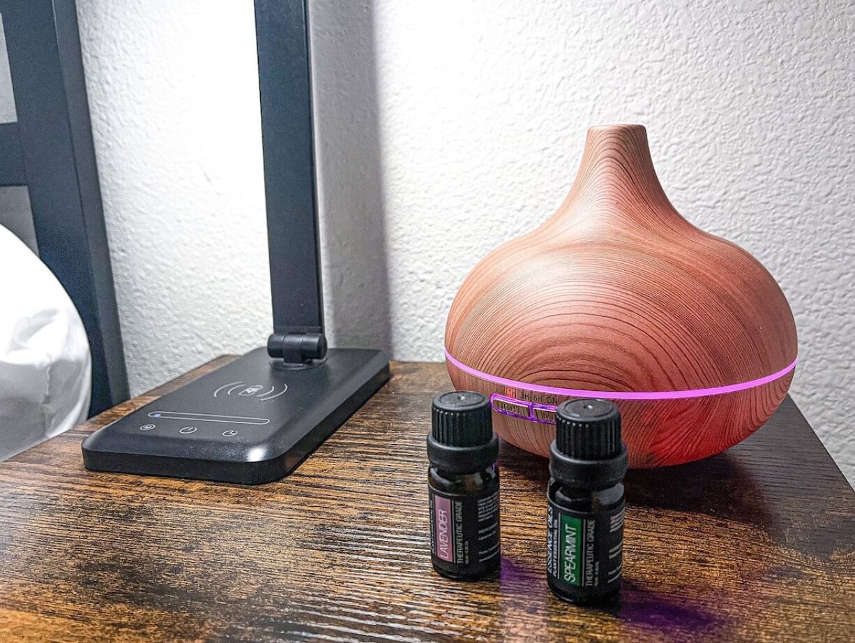 A diffuser with two bottles of essential oils and a wooden bowl on a wooden surface.