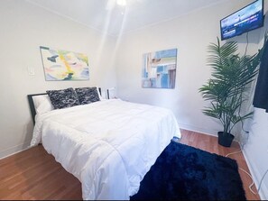 Une chambre à coucher avec un lit, une télévision, une plante et des œuvres d’art accrochées aux murs.