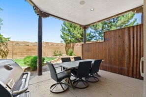 Une terrasse extérieure avec une table et des chaises, un barbecue et une clôture en bois.