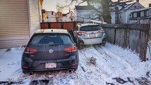 A residential driveway with two cars parked, a fence, and houses in the background. - Eastbayside/Munjoy - Charming Downtown Escape (Portland)