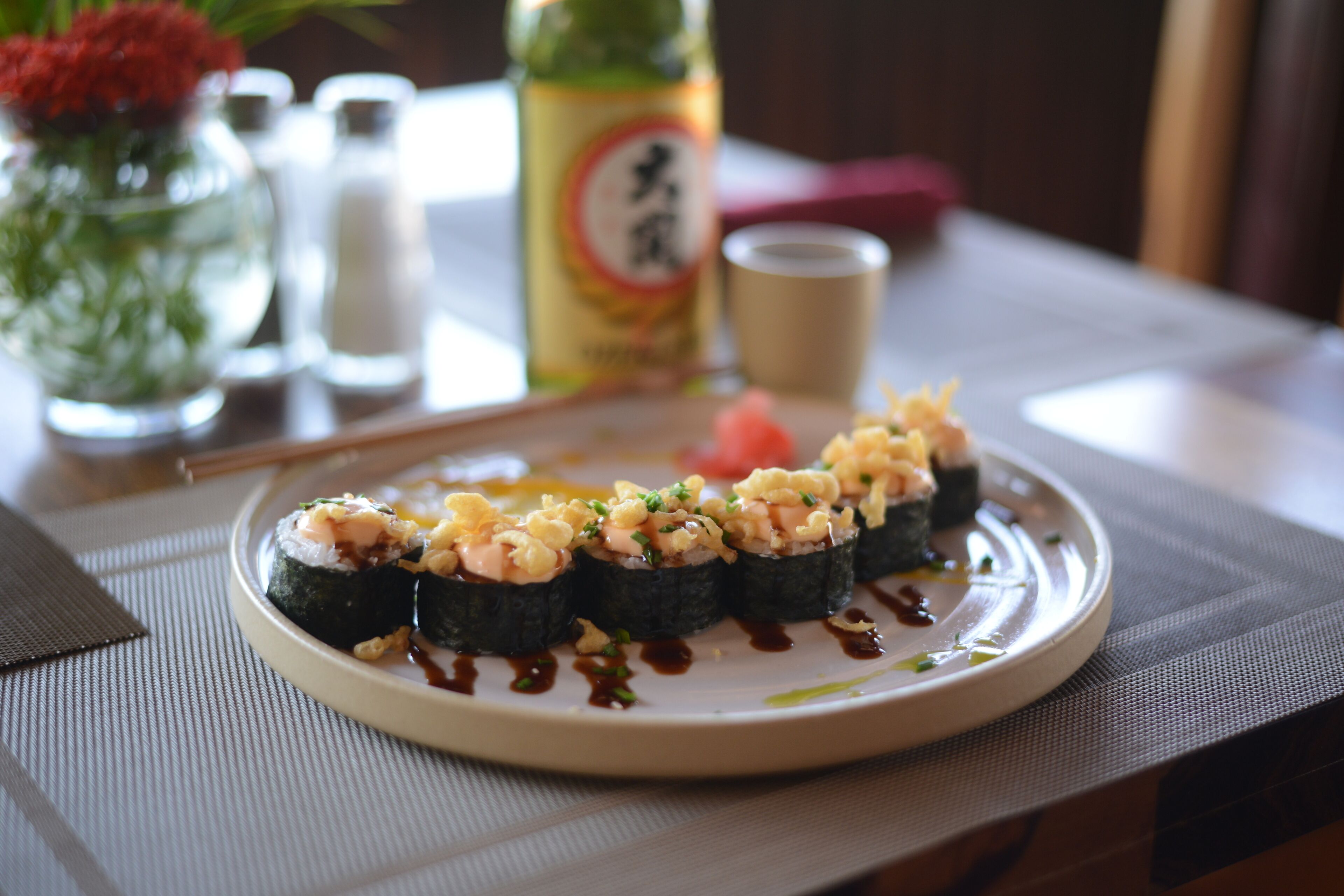 A plate of sushi on a table with a bottle and salt shakers in the background.
