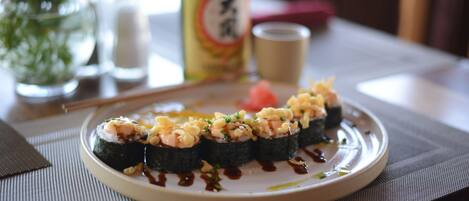 A plate of sushi on a table with a bottle and salt shakers in the background.