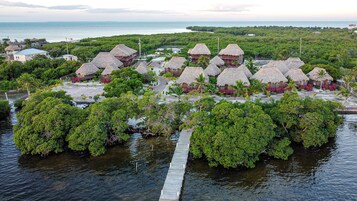 Un resort tropical con cabañas de techo de paja, un pasillo de madera sobre el agua y vistas al océano.