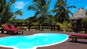 Una terraza de madera con piscina, sillas de descanso y palmeras.