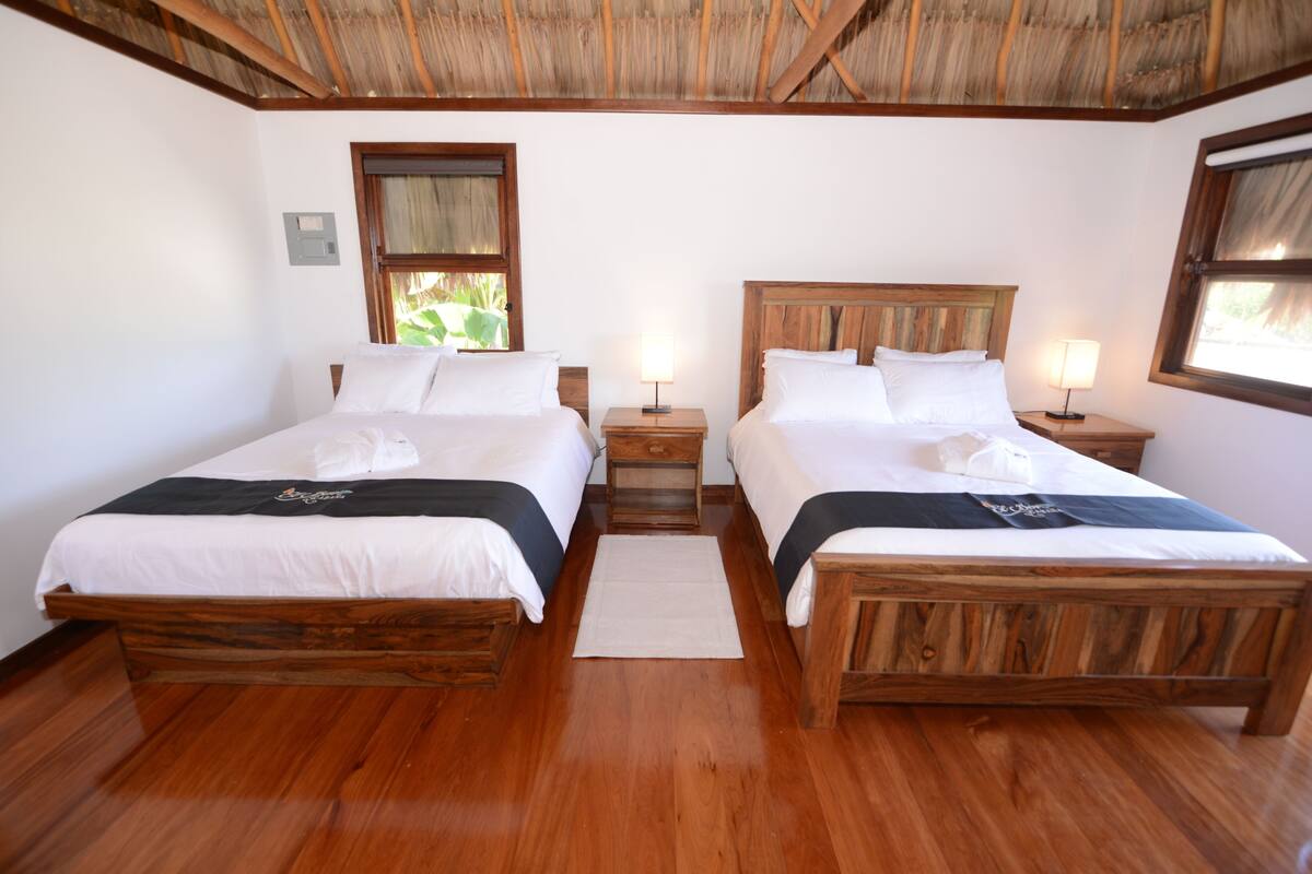 Una habitación con dos camas de madera, techo de madera y ventana con vista a la vegetación.