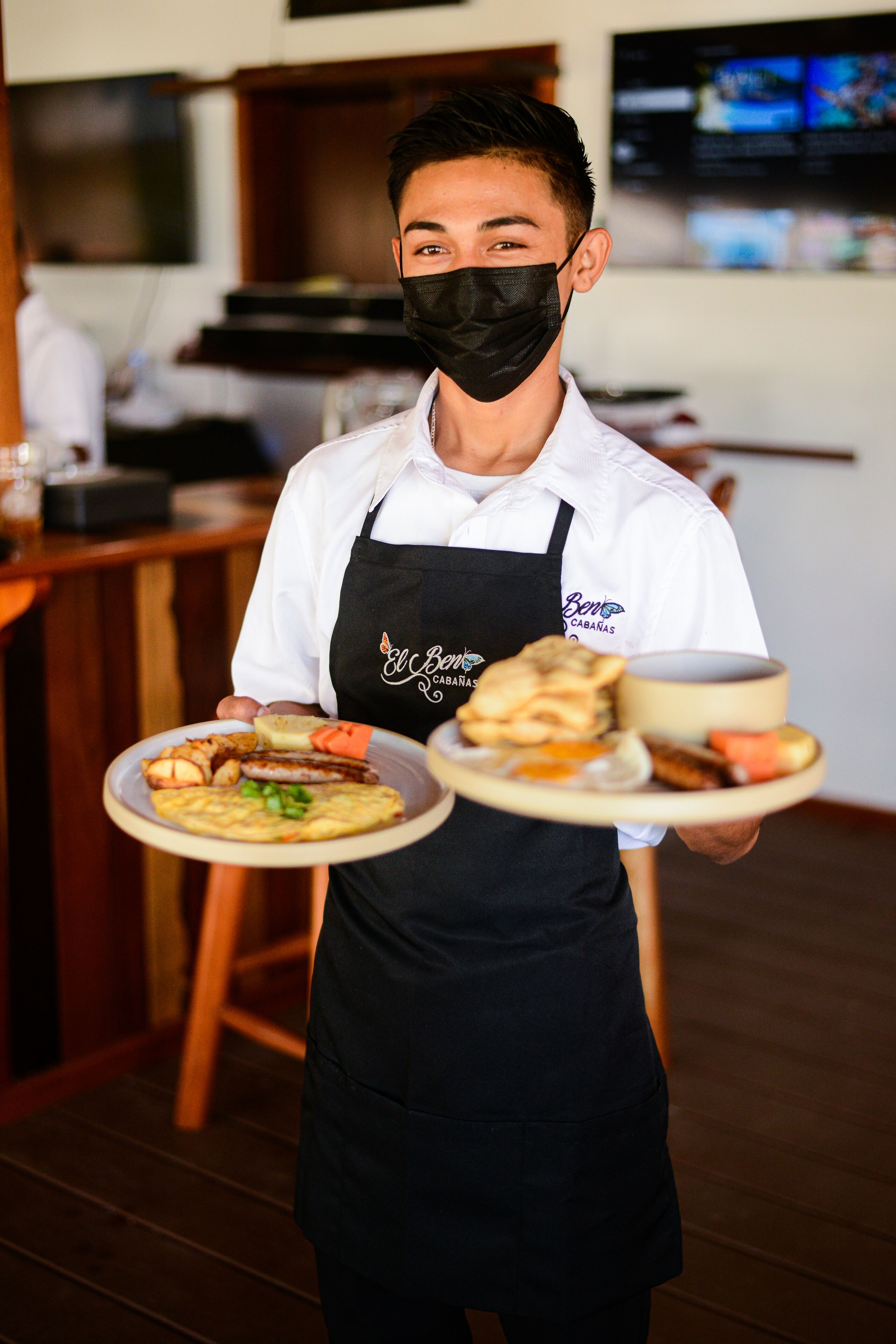 A person in a white shirt and black apron holding two plates of food.