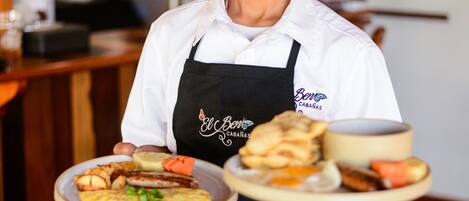 A person in a white shirt and black apron holding two plates of food.