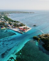 Vista aérea de un pueblo costero con una playa destacada, aguas azules cristalinas y embarcaciones visibles.