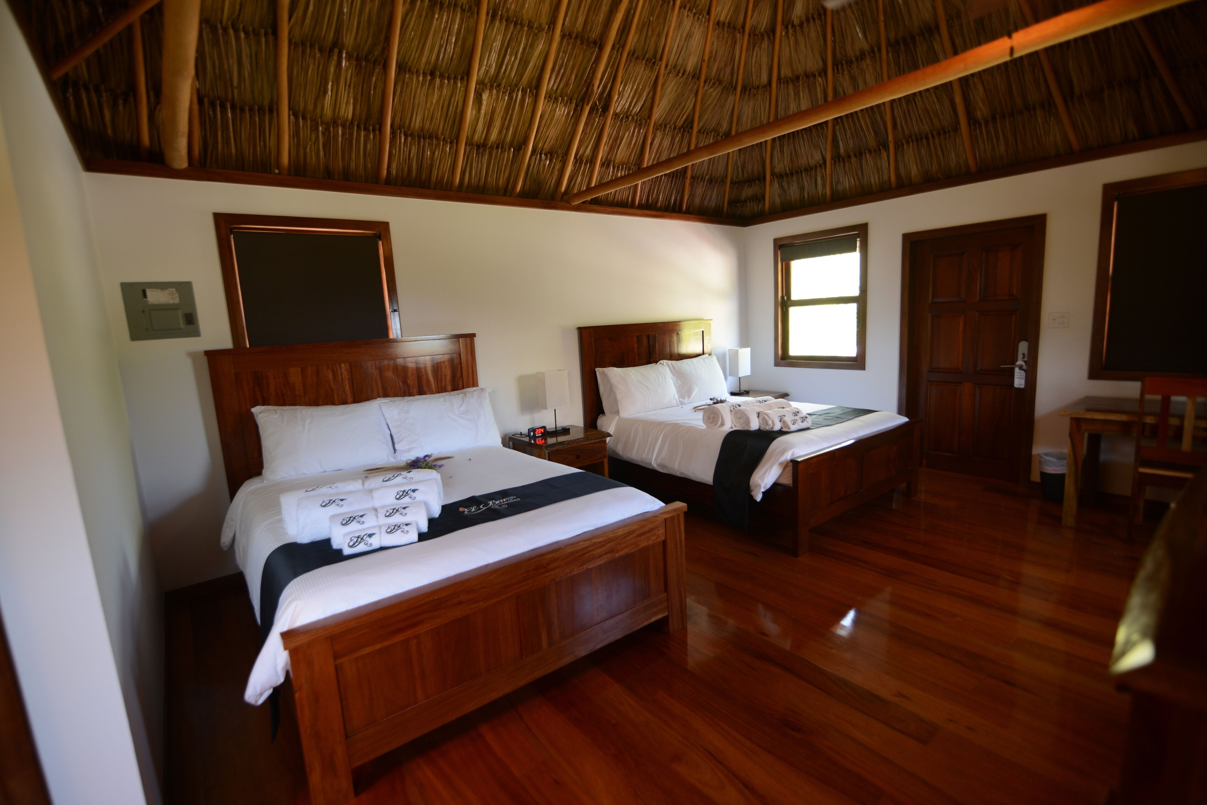A hotel room with two wooden beds, a thatched roof, and a wooden floor.