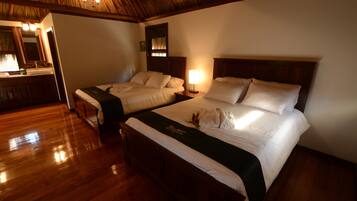 Habitación de hotel con dos camas, piso de madera, baño con espejo y lavamanos, y techo con vigas a la vista.