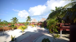 Un resort con estructuras de techo de paja, palmeras y un camino pavimentado.