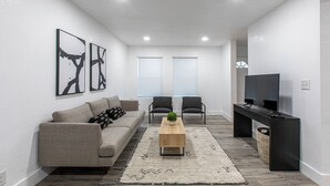 Una sala de estar moderna con un sofá, dos sillones, una mesa de centro y un televisor sobre un mueble.