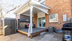 Un espacio de patio cubierto con terraza de madera, puerta corrediza de vidrio y una parrilla.