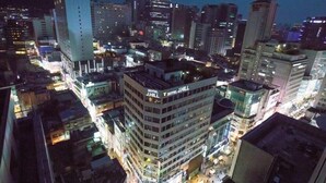 Un hôtel de grande hauteur, avec de nombreux étages, une enseigne bien visible et situé dans un quartier urbain animé, entouré d’autres immeubles et de rues.