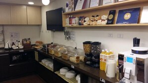 Un comptoir de petit-déjeuner avec divers aliments, une machine à café et une étagère où sont exposés des trophées et des ours en peluche.