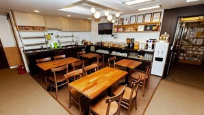 A restaurant with wooden tables and chairs, a kitchen area with appliances, and a display of food items. - Step Inn Myeongdong 2 (Seoul)