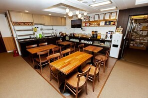 A restaurant with wooden tables and chairs, a kitchen area with appliances, and a display of food items. - Step Inn Myeongdong 2 (Seoul)
