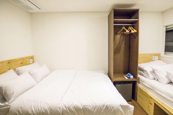 A hotel room with a large bed, a wooden wardrobe, and a small bedside table.