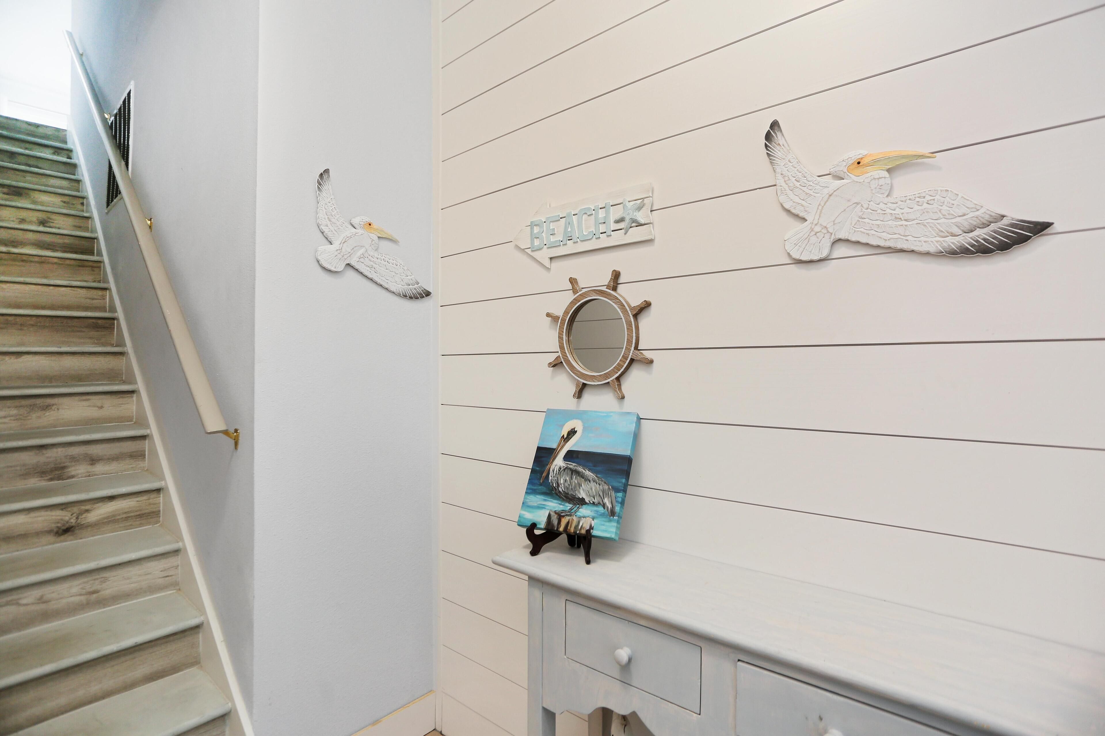A staircase with wooden steps and a white wall with nautical-themed decorations including a pelican, a ship's wheel, and a painting of a pelican.
