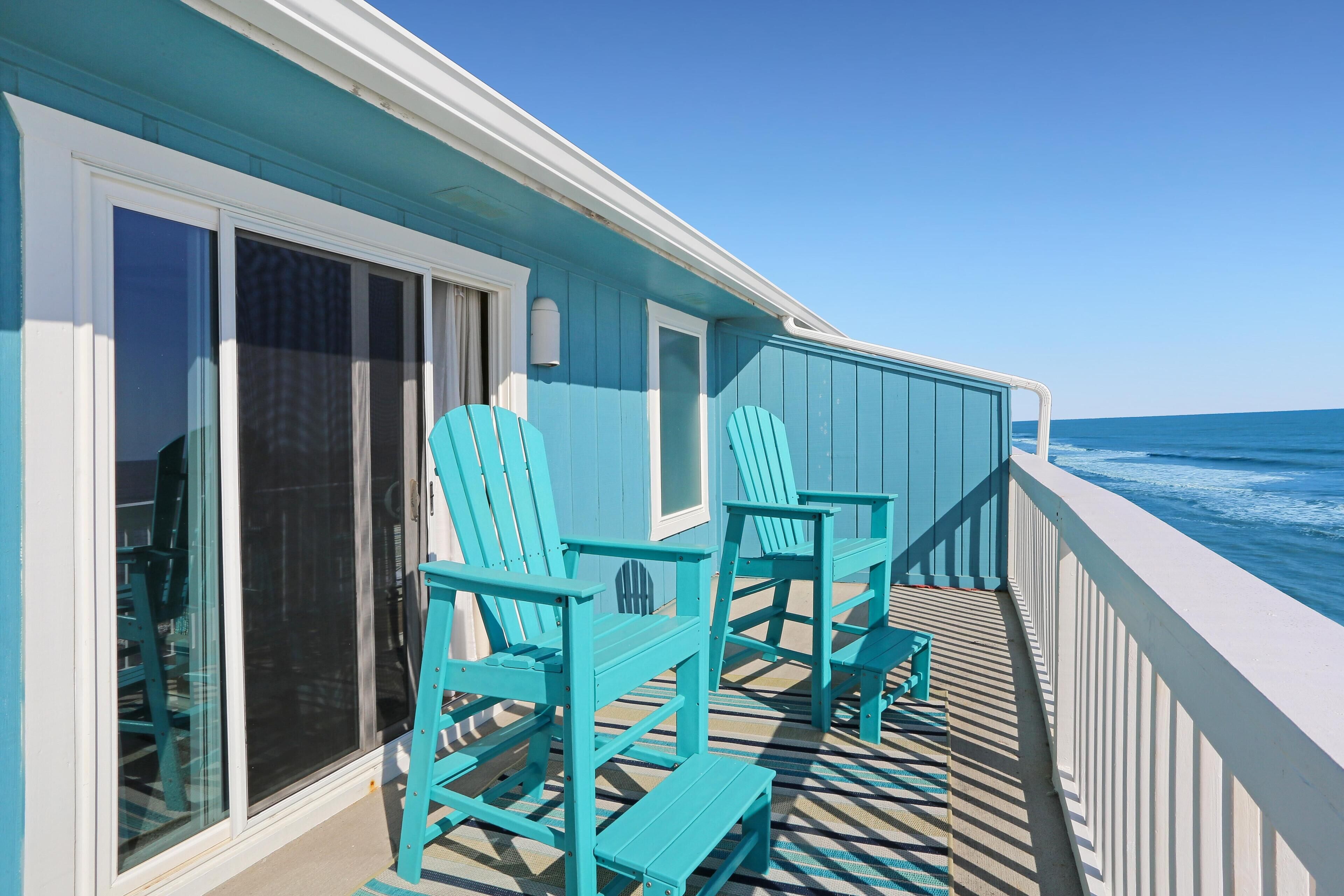 A balcony with turquoise Adirondack chairs and a view of the ocean.