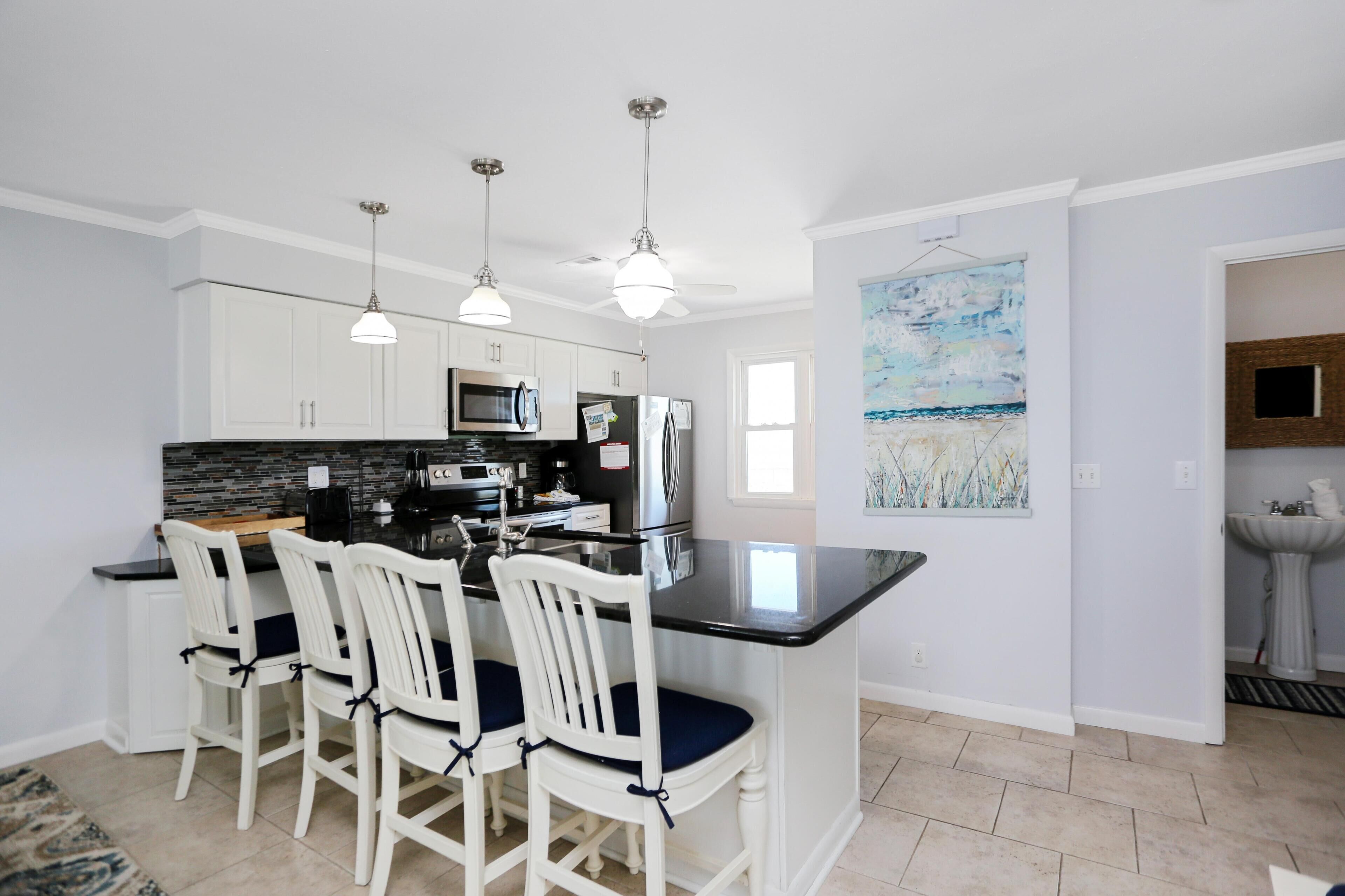 A modern kitchen with white cabinetry, a black countertop, and three pendant lights.