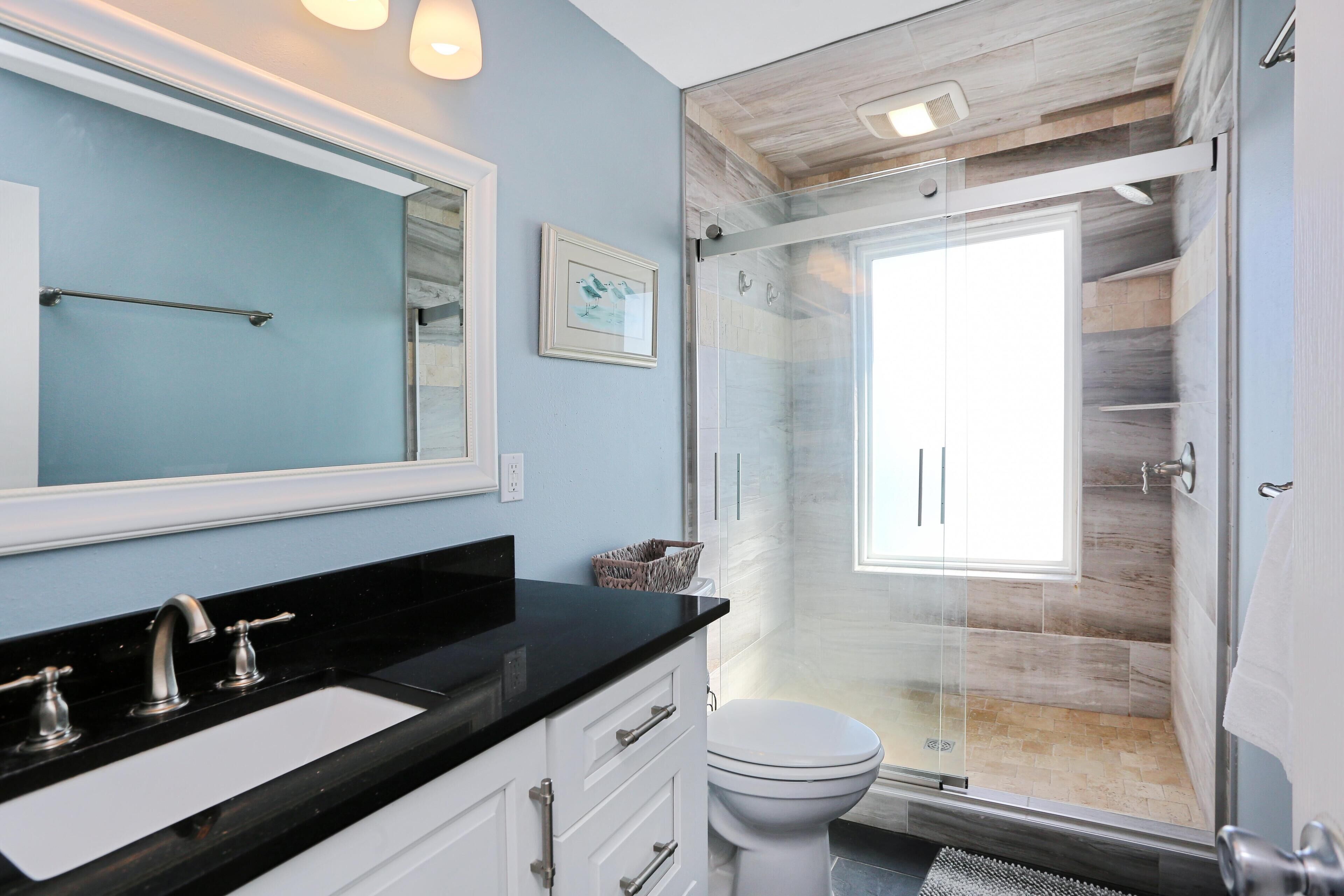 A modern bathroom with a black countertop sink, white cabinets, a glass shower enclosure, and a large mirror.