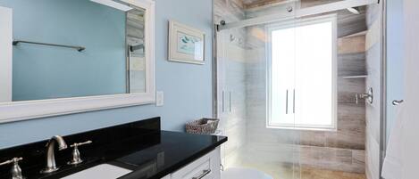 A modern bathroom with a black countertop sink, white cabinets, a glass shower enclosure, and a large mirror.