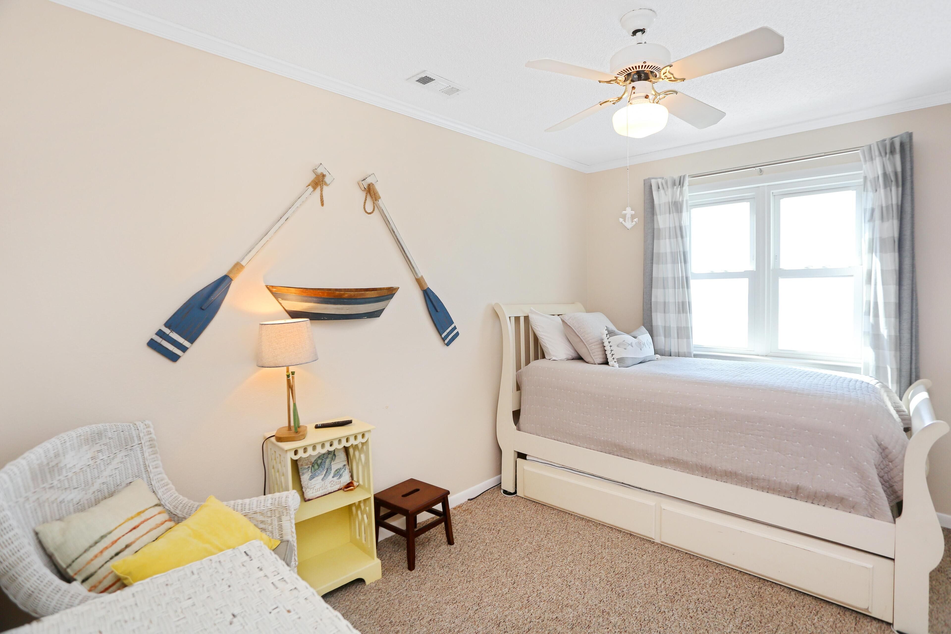 A bedroom with a bed, a chair, a small table, a lamp, and a ceiling fan.