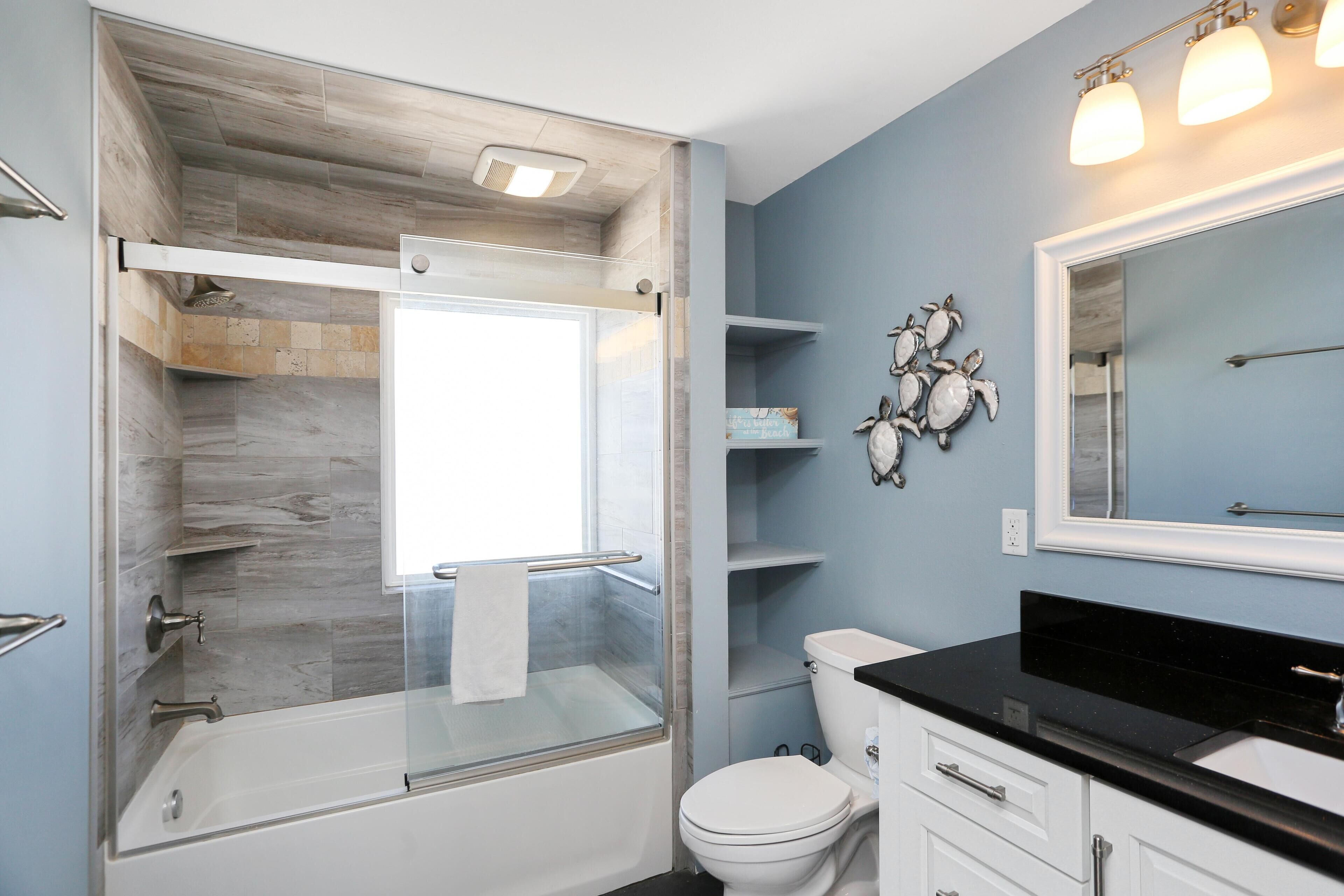 Une salle de bain moderne avec une douche à parois de verre, des toilettes blanches et un plan de toilette noir.