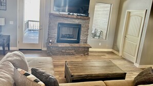 Ein Wohnzimmer mit Kamin aus Stein, einem Flachbildfernseher, einem Couchtisch aus Holz und einem beigen Sofa.