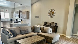 Ein modernes Wohnzimmer mit einem Ecksofa, einem Couchtisch aus Holz und einer Küche im Hintergrund.