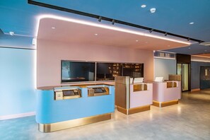 Un comptoir d’accueil doté d’un écran numérique, un espace salon et une bibliothèque dans le hall d’un hôtel moderne.