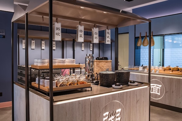 Un buffet proposant divers plats et ustensiles, un comptoir avec une machine à café, et des paniers suspendus en arrière-plan.