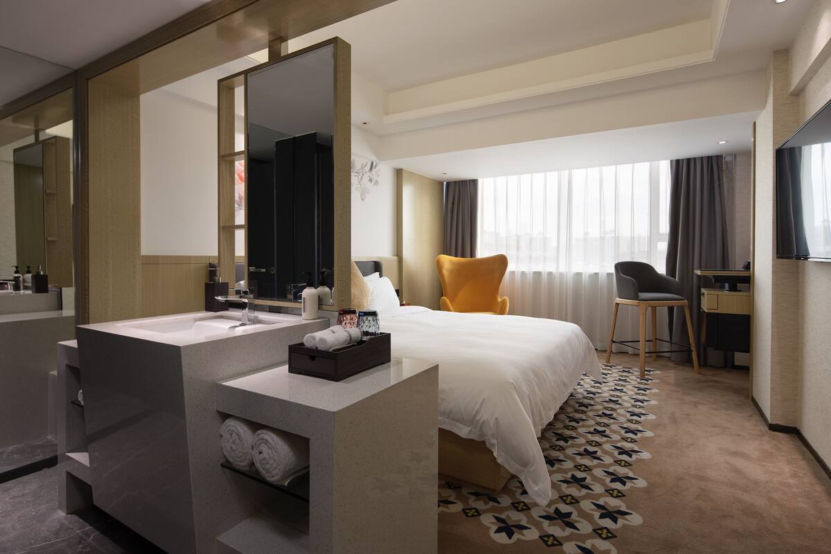 Une chambre d’hôtel moderne dotée d’un grand lit, d’un coin salon séparé, d’un bureau et d’une salle de bain avec un grand miroir et un lavabo.