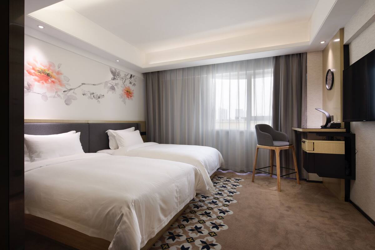 Une chambre d’hôtel avec deux lits, un bureau, une chaise, une télévision et un mur décoratif.