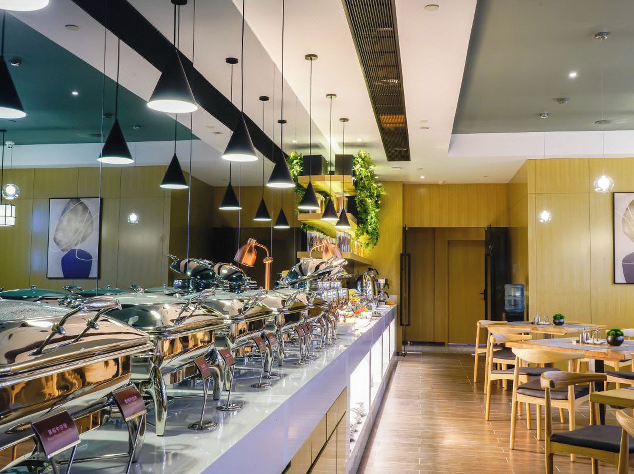 A buffet area with multiple food stations, hanging pendant lights, and a seating area with wooden tables and chairs.