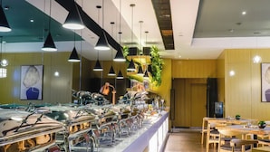Ein Buffetbereich mit mehreren Speiseauslagen, hängenden Pendelleuchten und einer Sitzgelegenheit mit Holztischen und -stühlen.