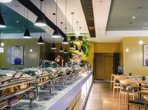 Un espace buffet comprenant plusieurs présentoirs de nourriture, des luminaires suspendus et un coin salon avec des tables et des chaises en bois.