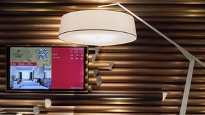 Una camera d'hotel moderna con una TV a schermo piatto che mostra informazioni sulla stanza, un'area salotto rotonda e un'elegante parete con listelli di legno orizzontali.