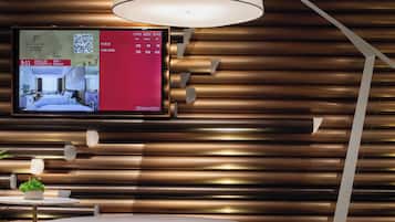 Quarto de hotel moderno com televisão de tela plana na parede, área de estar circular e abajur.