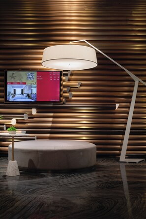 Ein modernes Hotelzimmer mit einem Flachbildfernseher, der Zimmerdetails anzeigt, einer runden Sitzecke und einer stilvollen Wand mit horizontalen Holzlatten.