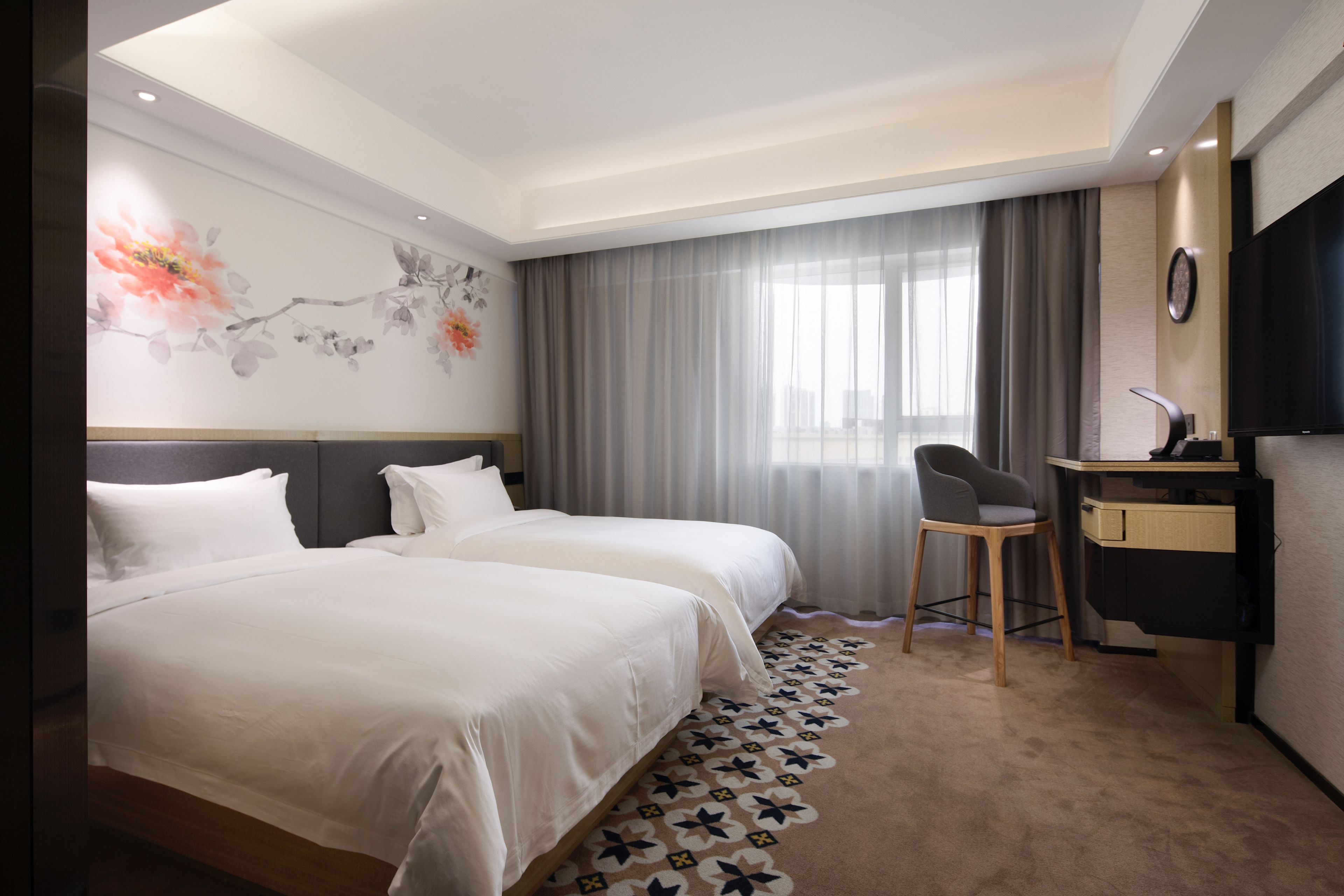 A hotel room with two beds, a desk, a chair, a TV, and a decorative wall.
